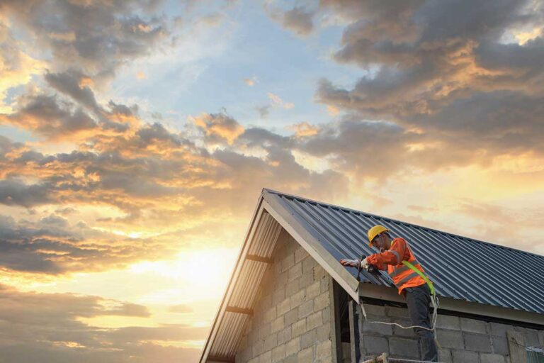 A worker installing new shingles on a sloped residential roof under clear daylight.