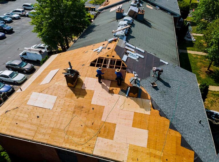 Homeowner reviews roof damage photos and insurance papers at a kitchen table after a storm.